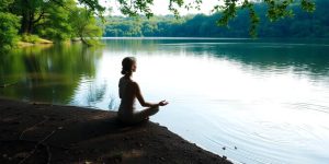 Person meditating by a calm lake in nature.